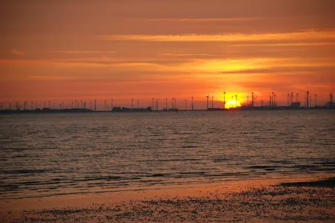 Sonnenuntergang am Emden Strand mit Windrädern und glitzerndem Wasser.