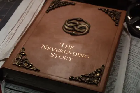 Brązowa księga z napisem "The Neverending Story" i wężami oplatającymi się na okładce.