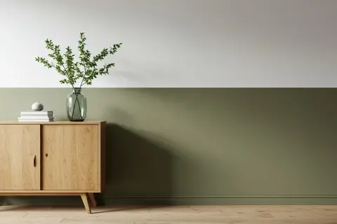 Eine zweifarbige Wand in Weiß und Olivgrün, akzentuiert durch ein Holzsideboard mit Vase und Büchern.