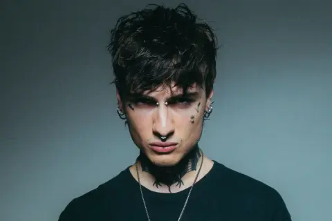 Giovane uomo con piercing e tatuaggi, sguardo intenso, un'aura che ricorda la **rosa chemical**.
