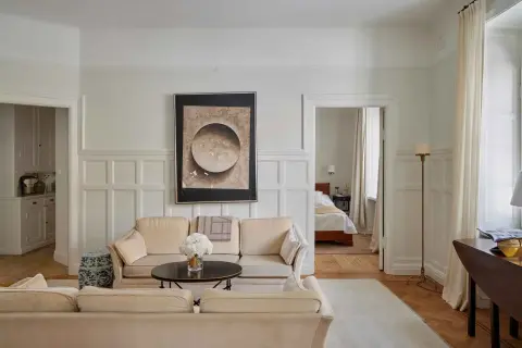 Vardagsrum med beigefärgad soffa, konstverk och en öppen dörr till sovrum. En vacker renovering av ett sekelskifteshus.