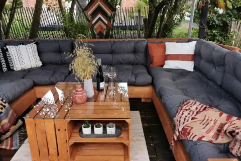 Gemütliches Palettensofa bauen: Eine Lounge-Ecke im Garten mit Glas-Couchtisch, Kissen und Decken. Perfekt für entspannte Stunden.