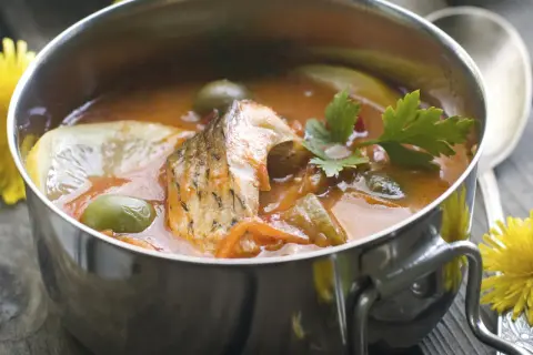 Aromaticzna rosyjska zupa rybna z kawałkami ryby, oliwkami, cytryną i natką pietruszki w metalowej misce.