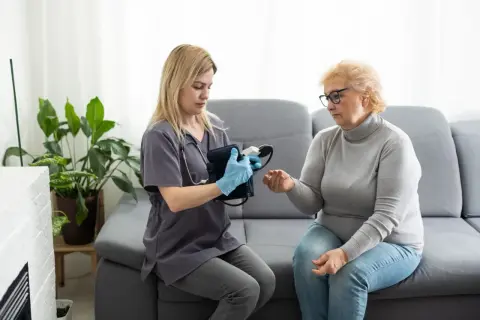 Pielęgniarka wykonuje wizyty domowe NFZ, mierząc ciśnienie starszej pacjentce.
