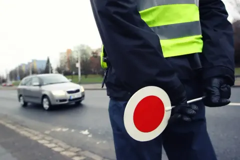 Agent de police en uniforme, gilet fluorescent, tenant un panneau stop. Contrôle routier, papier obligatoire.