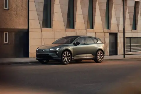Elegante Volvo EX60 verde metallizzato parcheggiata davanti a un edificio moderno con facciata geometrica.