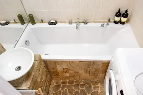 Badezimmer mit Waschbecken, Badewanne verkleiden mit Naturstein und Waschmaschine.