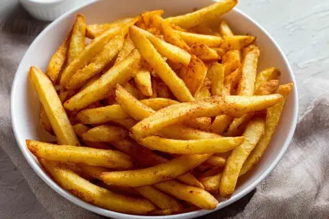 Chrupiące frytki z airfryer, posypane przyprawami, w białej misce. Idealna przekąska na szybki obiad.