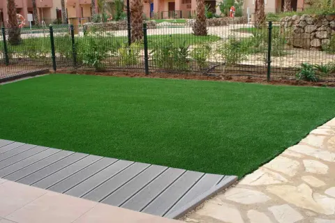Césped artificial verde vibrante junto a una terraza de madera gris. El césped artificial puede generar electricidad estática.