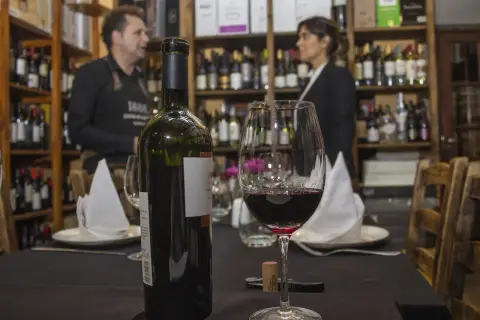 Butelka i kieliszek wina gruzińskiego, w tle sprzedawca w sklepie z winami w Tbilisi.