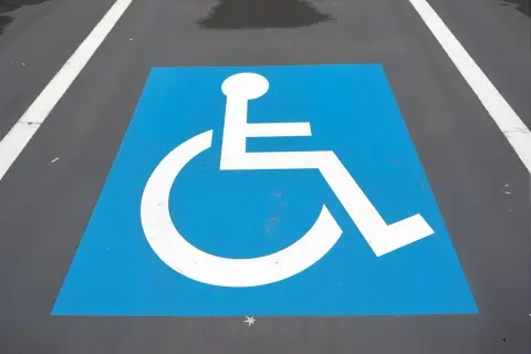 Symbole de fauteuil roulant blanc sur fond bleu, marquant une place de stationnement réservée. Une amende place handicapé est une infraction.