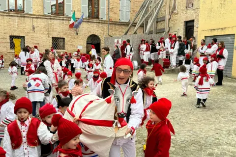 Un uomo con un costume da toro guida una sfilata di bambini vestiti di rosso e bianco per il carnevale nelle Marche.