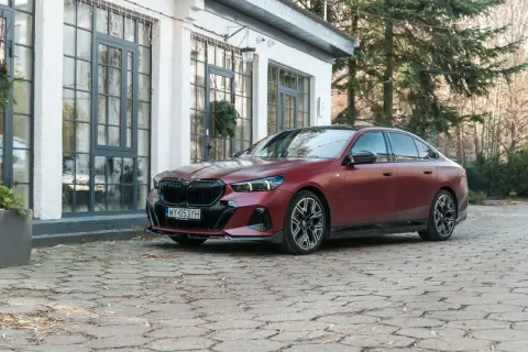 Elegancki, bordowy BMW 550e na brukowanym podjeździe przed nowoczesnym budynkiem.