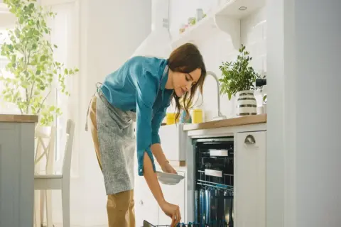 Kobieta wkłada talerz do zmywarki. Zastanawia się, czy lepsza będzie zmywarka 45 czy 60 cm.