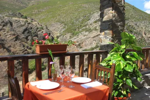 Mesa puesta para comer en Patones de Arriba, con vistas a un valle montañoso. Flores y plantas decoran el balcón.