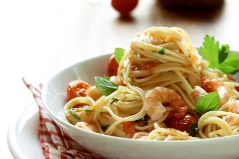 Ein Teller mit köstlichen Spaghetti mit Garnelen, Kirschtomaten und frischem Basilikum, appetitlich angerichtet.