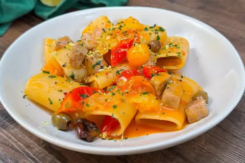 Paccheri con tonno fresco, pomodorini, olive e scorza di limone. Un piatto colorato e saporito, pronto per essere gustato.