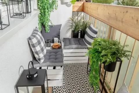 Przytulny balkon w bloku z wygodnymi siedziskami z palet, mnóstwem zieleni i czarno-białymi dodatkami. Idealne miejsce na poranną kawę.