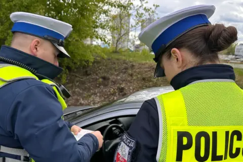 Policjanci w kamizelkach odblaskowych sprawdzają dokumenty, być może wystawiają mandaty za prędkość.