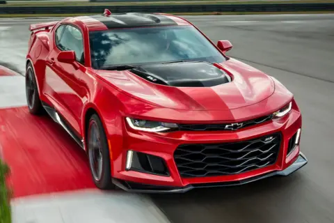 Czerwone Camaro ZL1 z czarnymi pasami na masce i dachu, pędzące po torze wyścigowym.