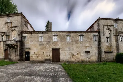 Las Torres de Allo, un edificio de piedra con un balcón ornamentado y ventanas blancas, se alza bajo un cielo nublado y dinámico.