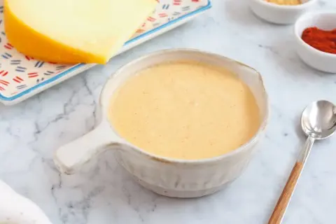 Crema de salsa de queso lista para servir, con un trozo de queso y especias al fondo.