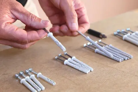 Man manipula un taco químico para pared, preparándolo para fijar algo.