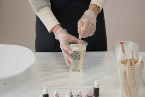 Mani guantate mescolano resina epossidica in un bicchiere, un passo fondamentale per imparare come usare la resina epossidica sul legno per creare opere d'arte uniche.