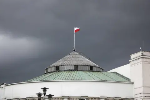 Polski parlament pod burzowym niebem. Biało-czerwona flaga powiewa na maszcie, symbolizując stan wyjątkowy w Polsce.