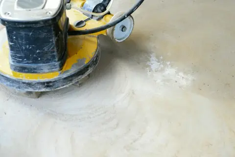 Maschine schleift Beton. Staub wirbelt auf, während die rotierende Scheibe den Boden glättet.