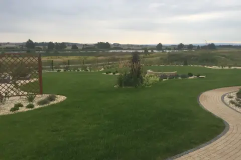 Zadbany ogród z trawnikiem, kamiennymi ścieżkami i rabatami. W tle jezioro i pola. Fosforan monopotasowy pomógł uzyskać tak piękny, zielony trawnik.