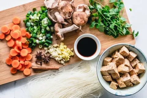 Co jedzą weganie? Tofu, makaron ryżowy, grzyby shiitake, marchew, szczypiorek, czosnek, imbir, kolendra, sos sojowy i przyprawy.