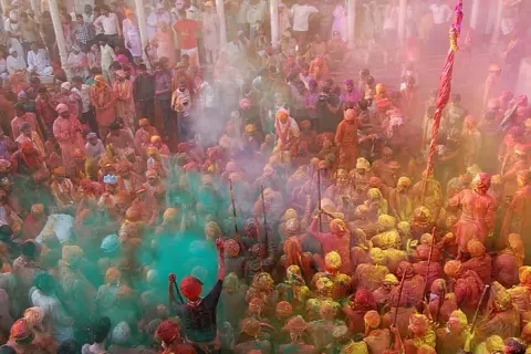 Tłum ludzi w kolorowych strojach, obsypany proszkami podczas święta Holi w Indiach.