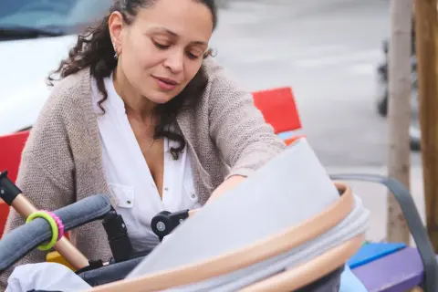 Kobieta po czterdziestce pochyla się nad wózkiem, przygotowując pierwsze dziecko do spaceru.