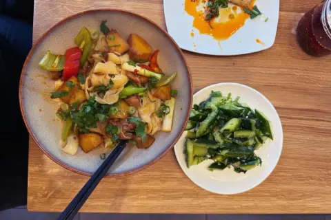 Ein Teller mit Nudeln, Kartoffeln und Gemüse, daneben ein Schälchen mit Gurkensalat. Typisch chinesisches Essen, das zum Genießen einlädt.