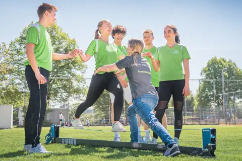 Junge Menschen üben auf einem Slackline-Parcours. Eine Dozentin unterstützt sie bei der physiotherapeutischen Ausbildung nebenberuflich.