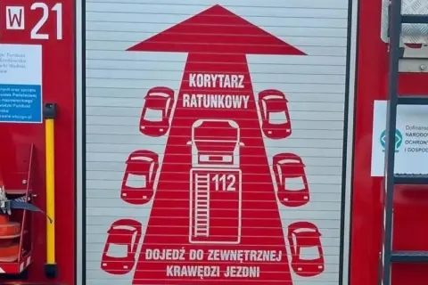 Grafika na drzwiach wozu strażackiego przedstawia korytarz życia, symbolizujący drogę dla pojazdów ratunkowych.