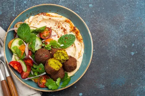 Pyszny falafel co to? Kulki z ciecierzycy z hummusem, świeżymi warzywami i miętą na talerzu.