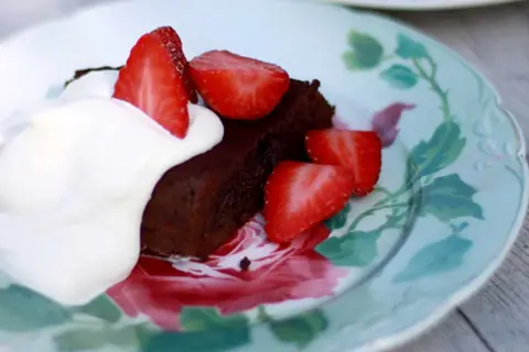 En bit fransk chokladtårta med vispgrädde och färska jordgubbar på en vacker tallrik med blomstermönster.