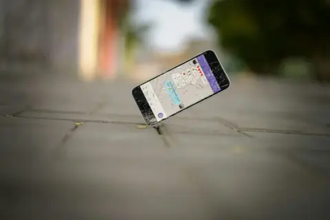 Zgubiony telefon z pękniętym ekranem leży na chodniku. Na wyświetlaczu widać wiadomość: "Did you just break up w/ me?".