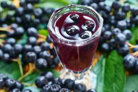 Aronia w kieliszku, otoczona świeżymi owocami i liśćmi. To nalewka z aronii przepis babci, pełna smaku i zdrowia.