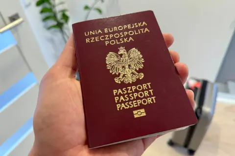 Dłoń trzyma polski paszport z godłem orła.
