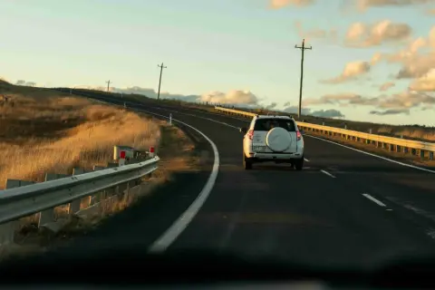 Biały SUV jedzie pustą drogą w Australii, otoczoną złotymi trawami i słupami telegraficznymi. Ruch drogowy jest minimalny.