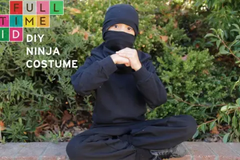 Dziecko w czarnym stroju ninja siedzi na ziemi, ręce złożone w geście.