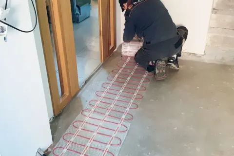 Instalator układa matę grzewczą, przygotowując ogrzewanie podłogowe elektryczne.