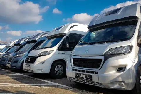Rząd kamperów na parkingu, idealny na wakacje. Szukasz kamper tanio? Te pojazdy czekają na Ciebie!
