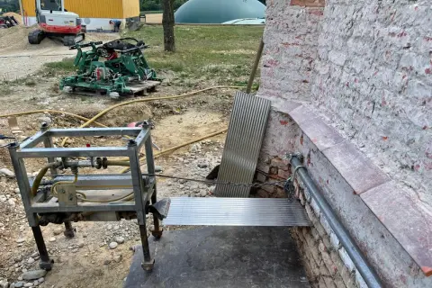 Baustelle mit Bagger, Maschine und Metallkonstruktion. Eine horizontale Sperrschicht aus Metallblech schützt die Ziegelwand.