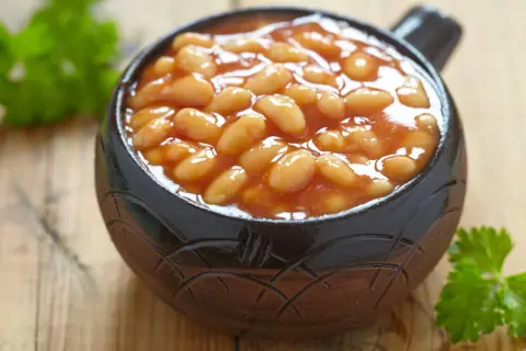 Un bol de haricot blanc en sauce tomate, garni de persil frais, sur fond de bois.