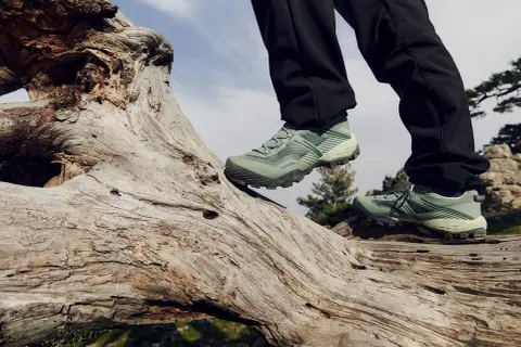 Zielone buty trekkingowe na pniu drzewa. Idealne, by wybrać się na wędrówkę po górach.