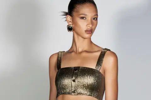 Modella con bronzer come si usa per un look radioso. Capelli raccolti, top dorato e orecchini neri.